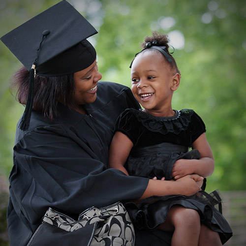 Female graduate in regalia holding daughter.
