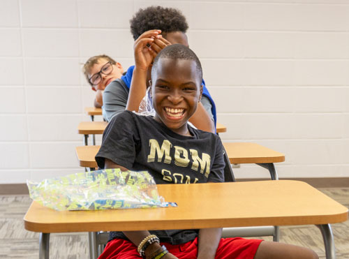 Foundation Camp camper laughing, sitting in a school desk