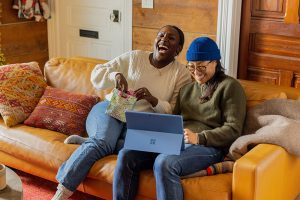 two women laughing as they open a gift and look at a laptop