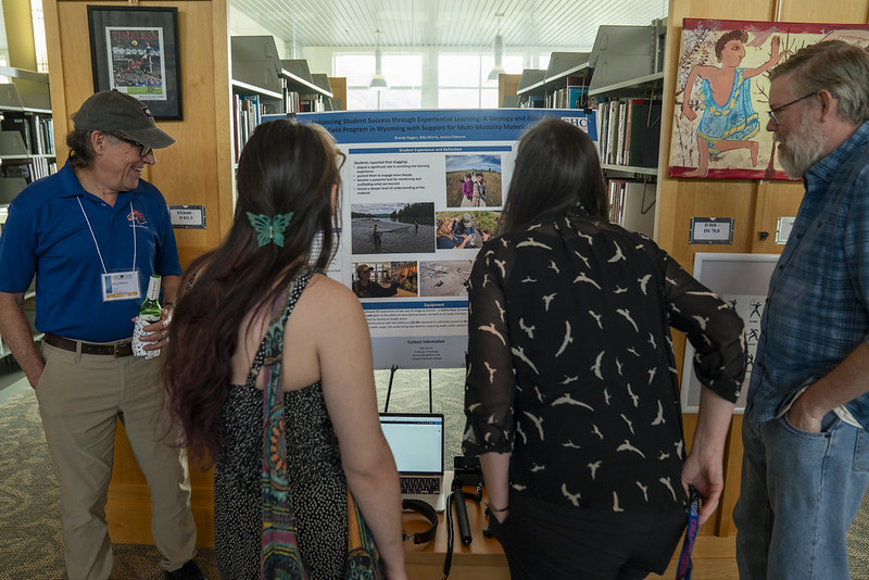 A professor talks to a group of colleagues about a poster.