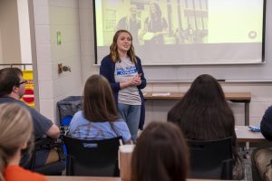 A woman presents to a small audience in a classroom. 
