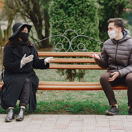 young couple in protective gloves and masks chatting in park