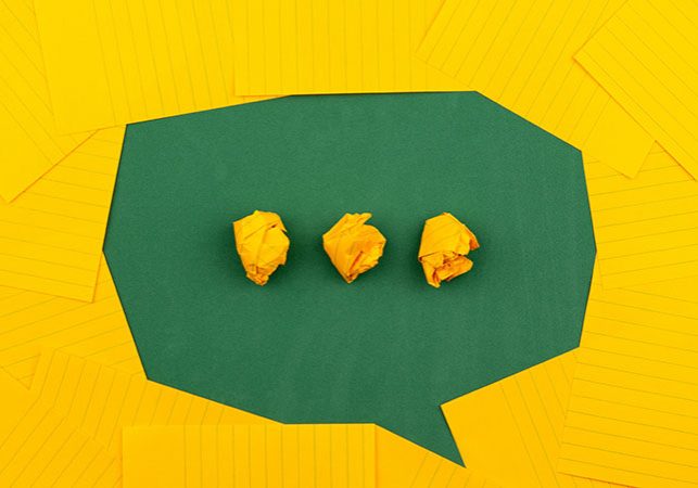 three crumpled yellow papers on green surface surrounded by yellow lined papers in shape of speech bubble