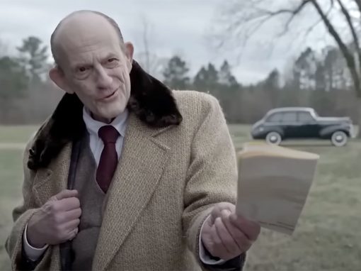 Christopher Lloyd in suit holding paper toward someone off-screen.
