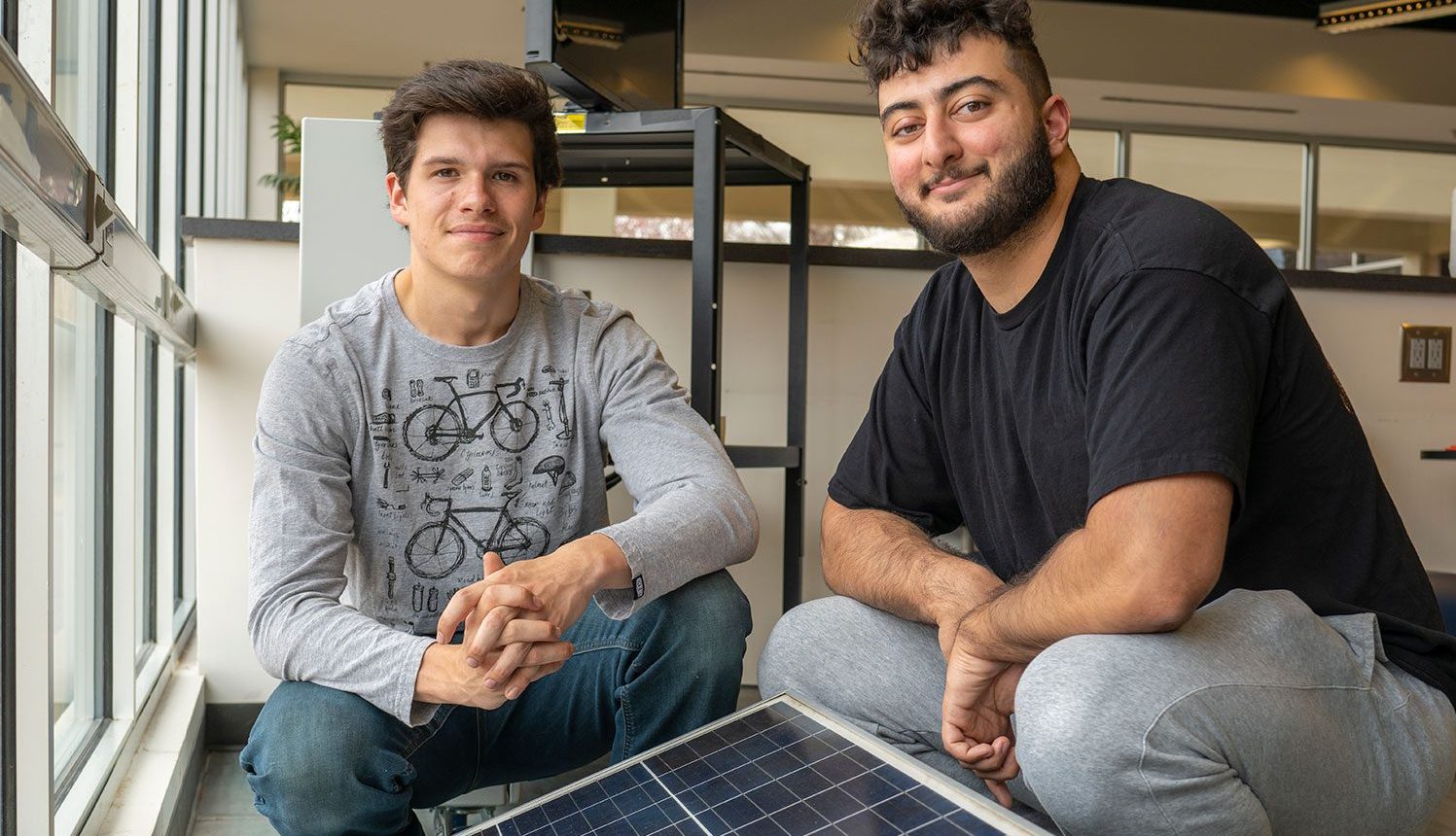 Jayem Odeh and Spencer Bush sitting beside a row of solar panels