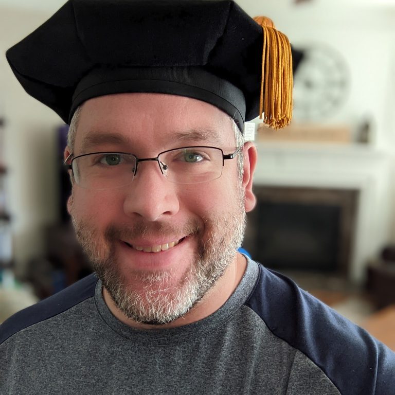 tam white man with graying beard wearing PhD tam and baseball tshirt
