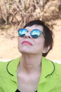 Image of a woman in a lime green jacket staring up at a partly cloudy sky with reflective sunglasses