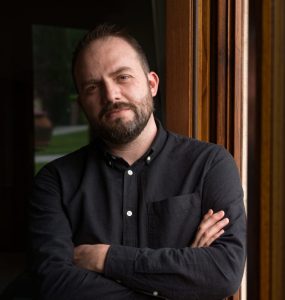 Photo of a man with a beard standing in a doorway with his arms crossed