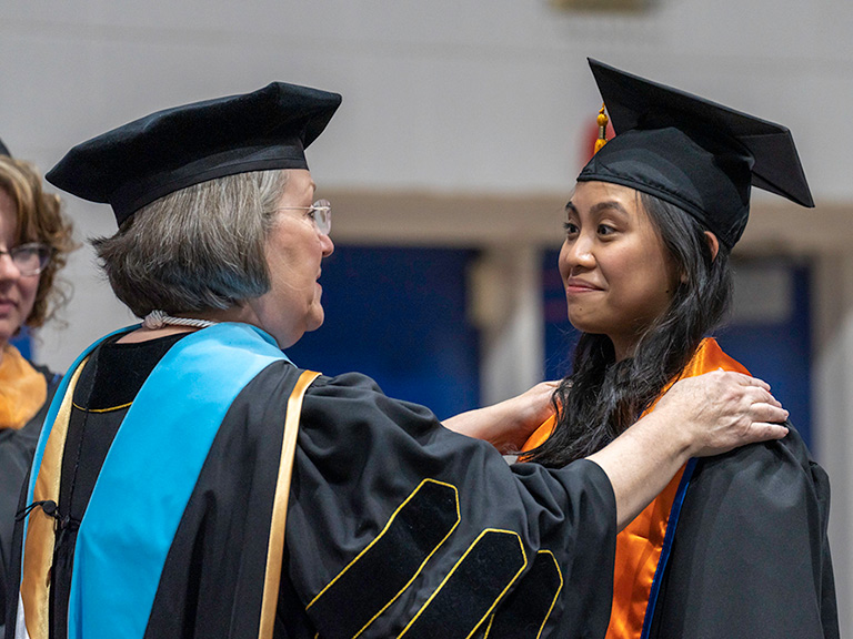 Faculty member speaking to female student with hands on student's shoulders at graduation
